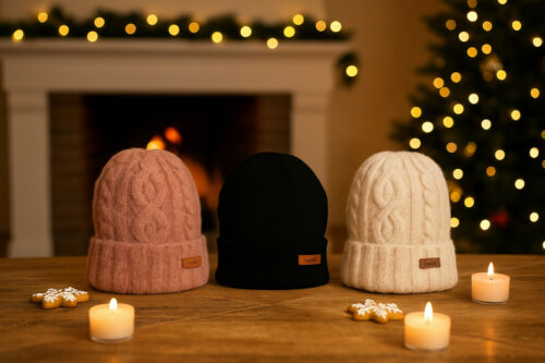 dit zijn drie mutsen de linker is rood die in het middel is zwart en de rechter is beige de mutsen staan op tafel voor een versierde openhaard en rechts in de hoek staan een versierde kerstboom en op de tafel liggen wat kaarsjes en kerstkoekjes